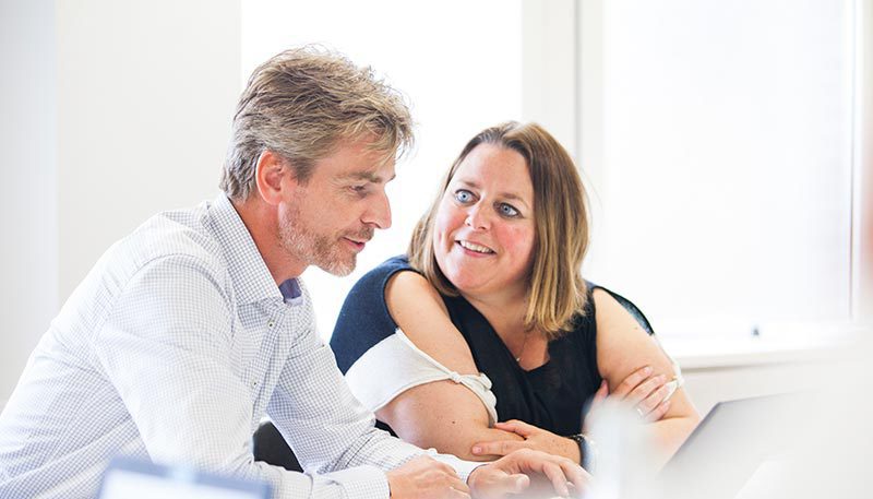 Collega's overleggen aan tafel, laptop open.