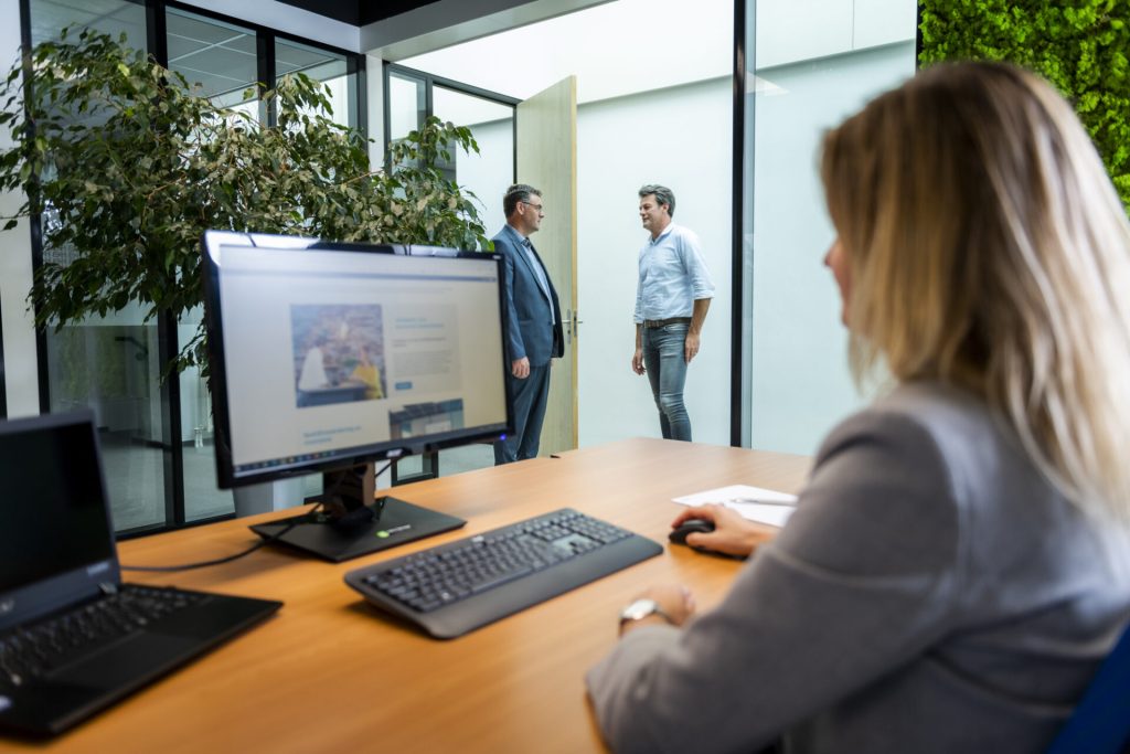 Persoon werkt aan bureau; gesprek in gang zichtbaar.