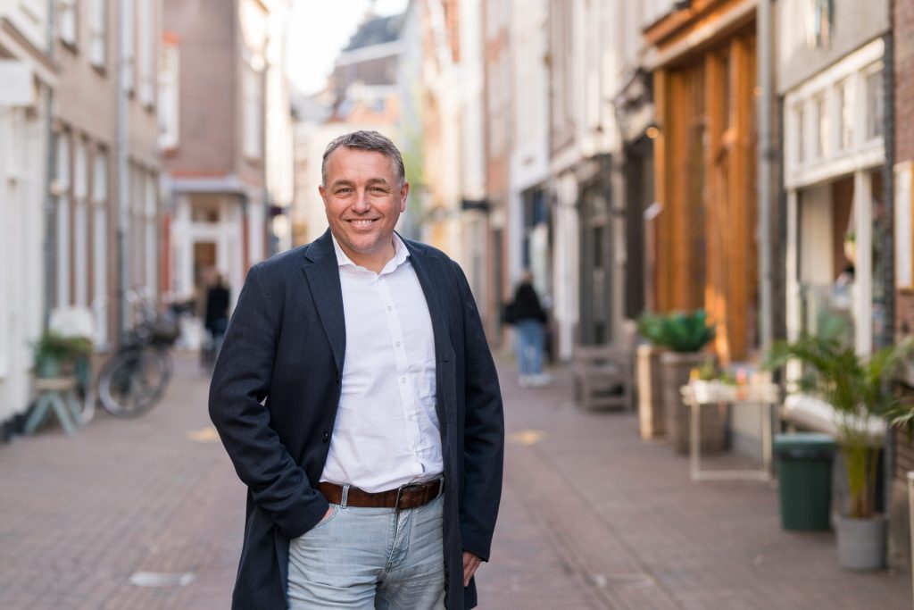 Man in straat met winkelpanden, lachend in camera