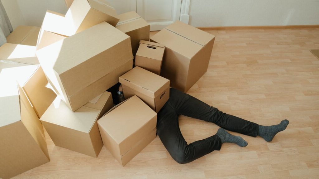 Persoon bedolven onder kartonnen dozen in kamer.