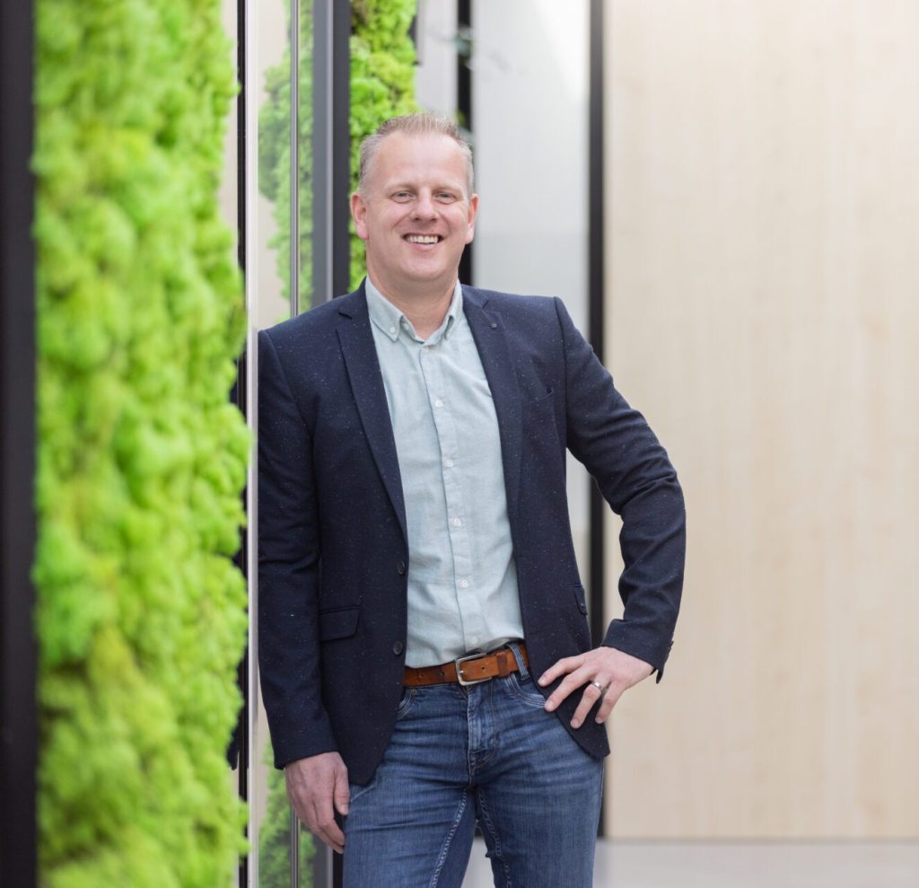 Person in blazer bij groene muur.