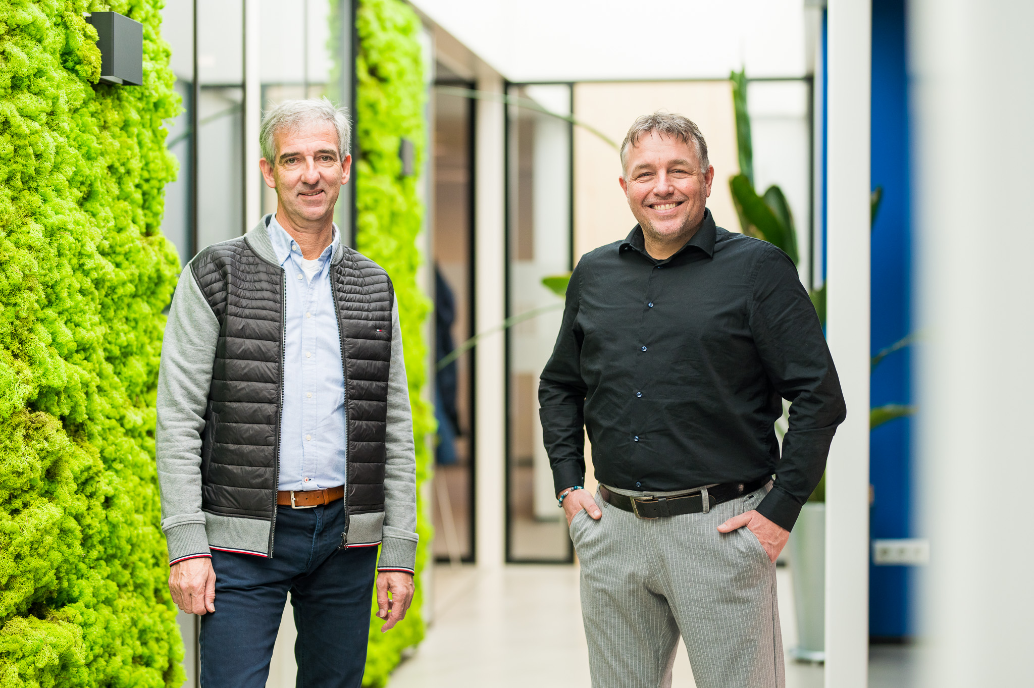 Twee mannen poseren in modern kantoor met groene muren.