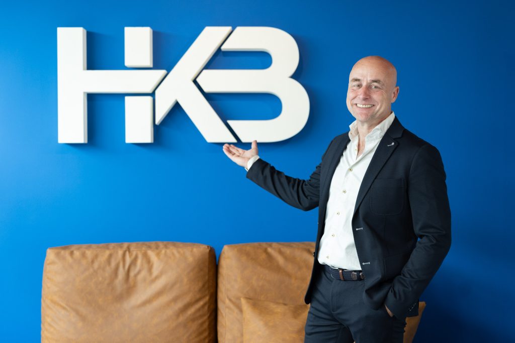 Man naast HK3 logo op blauwe muur