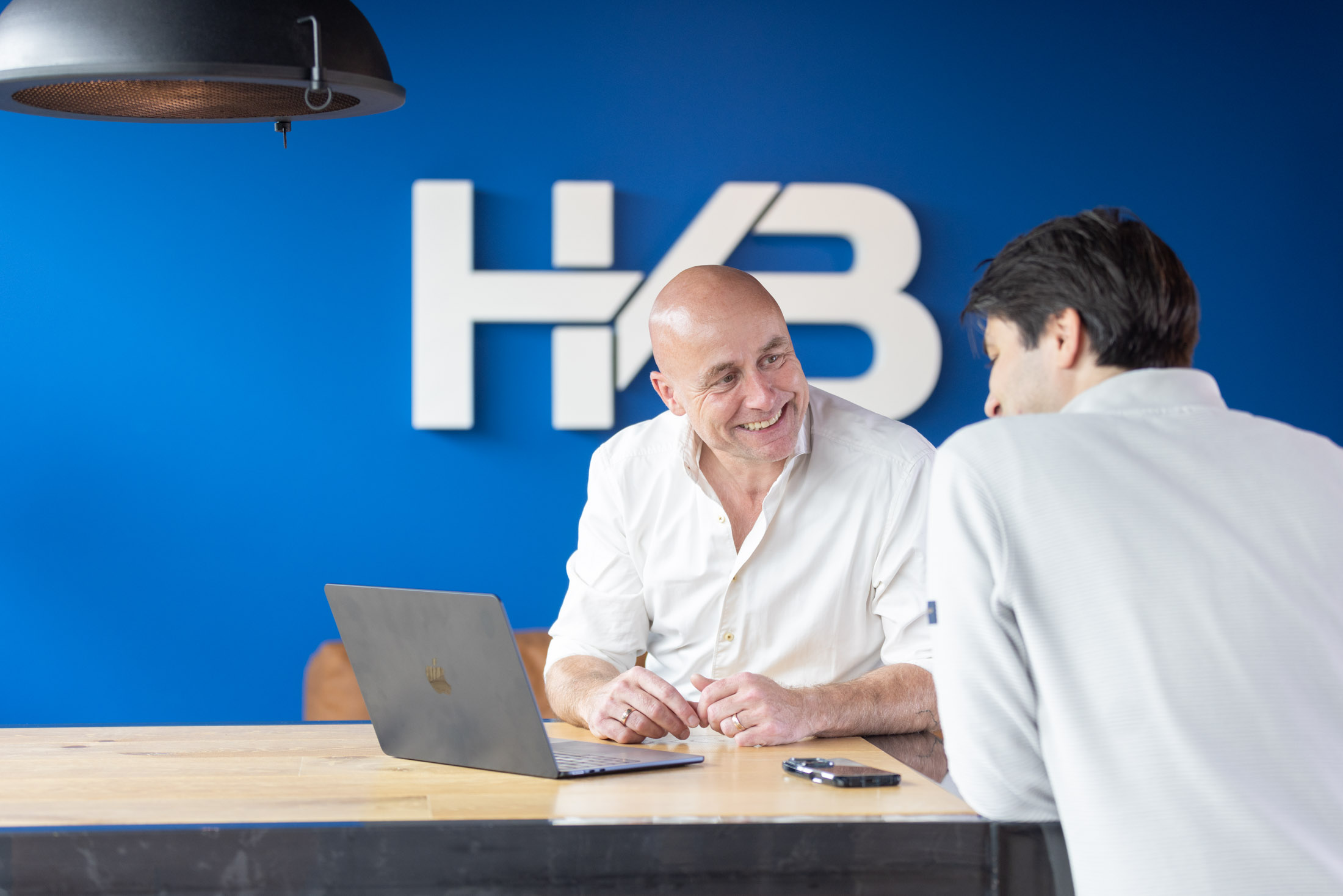 Twee mannen praten bij bureau met laptop.