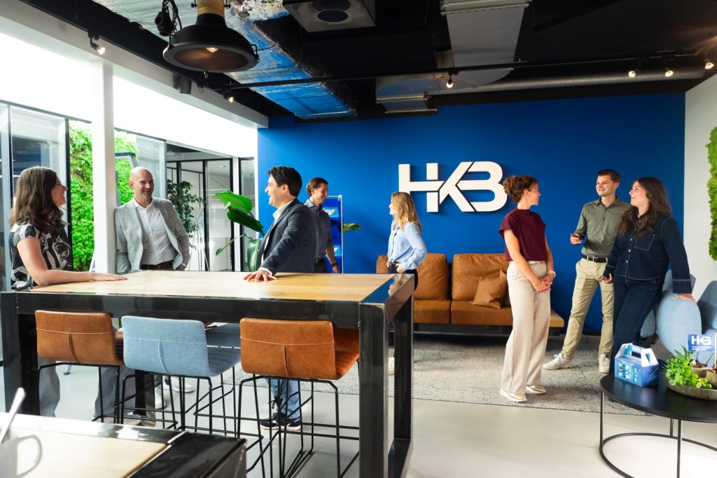 Mensen praten in kantoorruimte met HKB-logo.