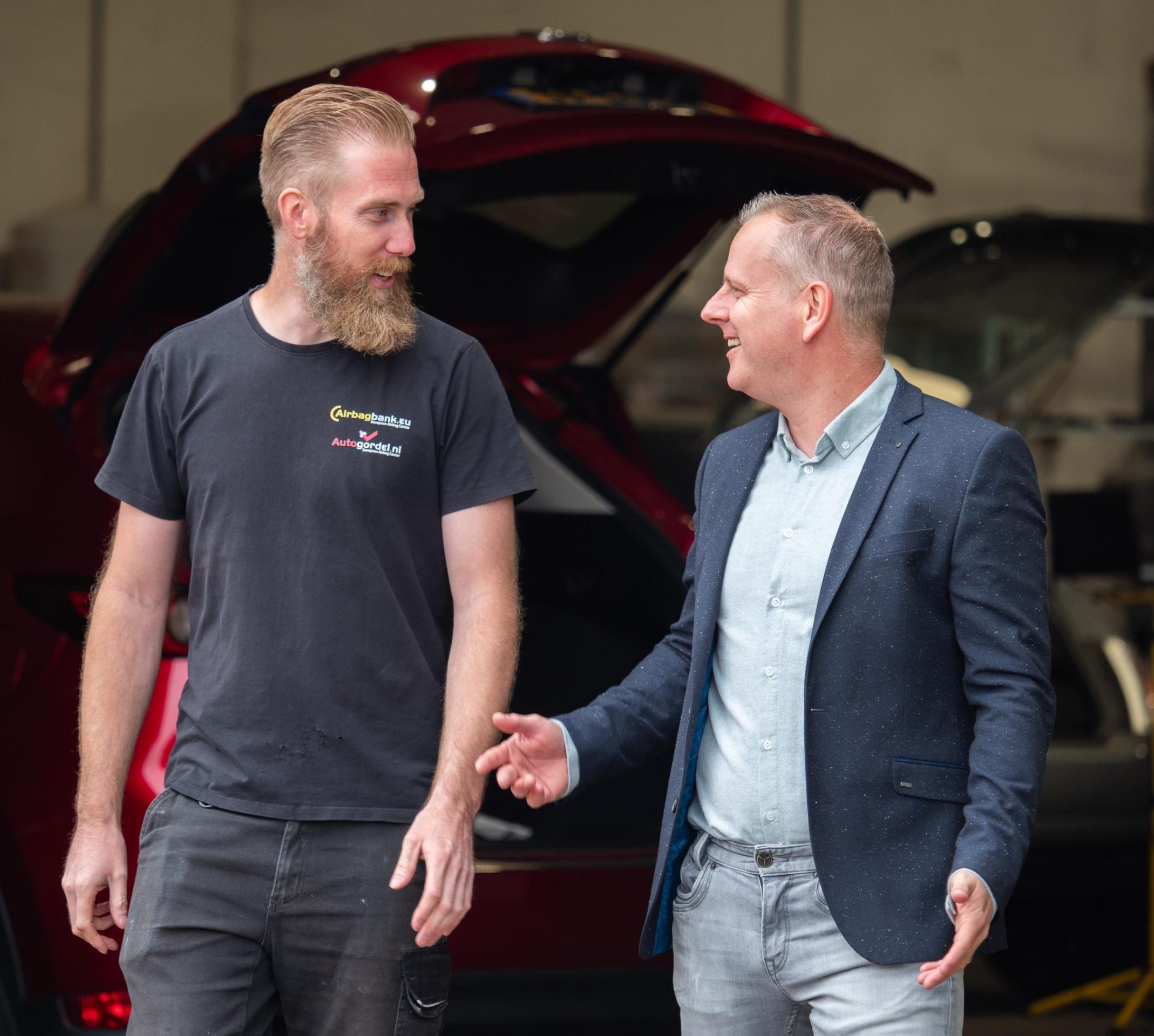 Twee mannen praten voor een geopende autokofferbak.
