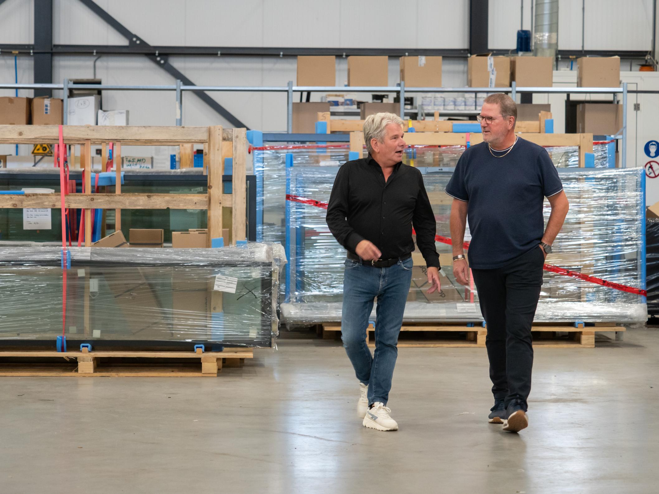 Twee mannen lopen pratend in een magazijn.