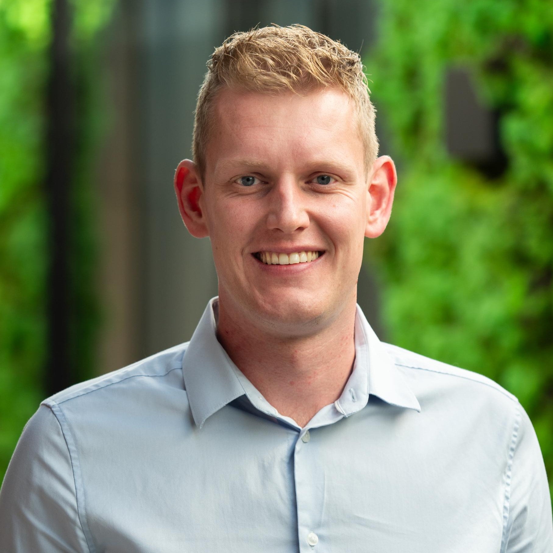 Lachende persoon met groene achtergrond, lichte overhemd.