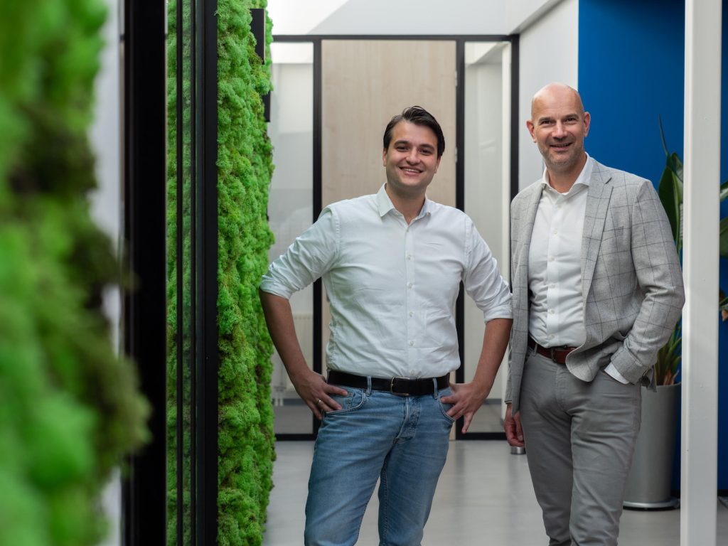 Twee mannen poseren in kantoor met groene plantenwand.