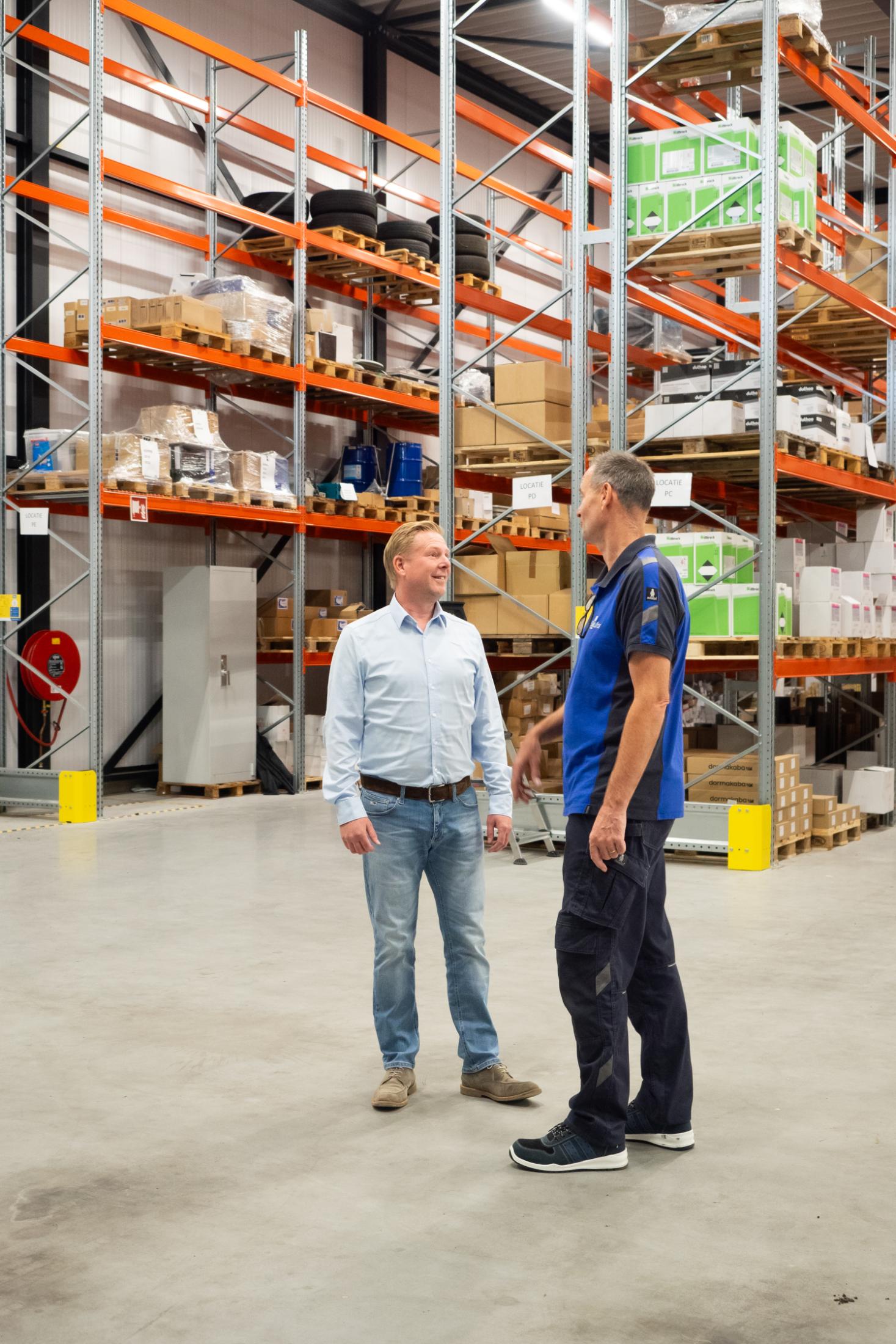 Twee mannen praten in opslagruimte met stellingen.