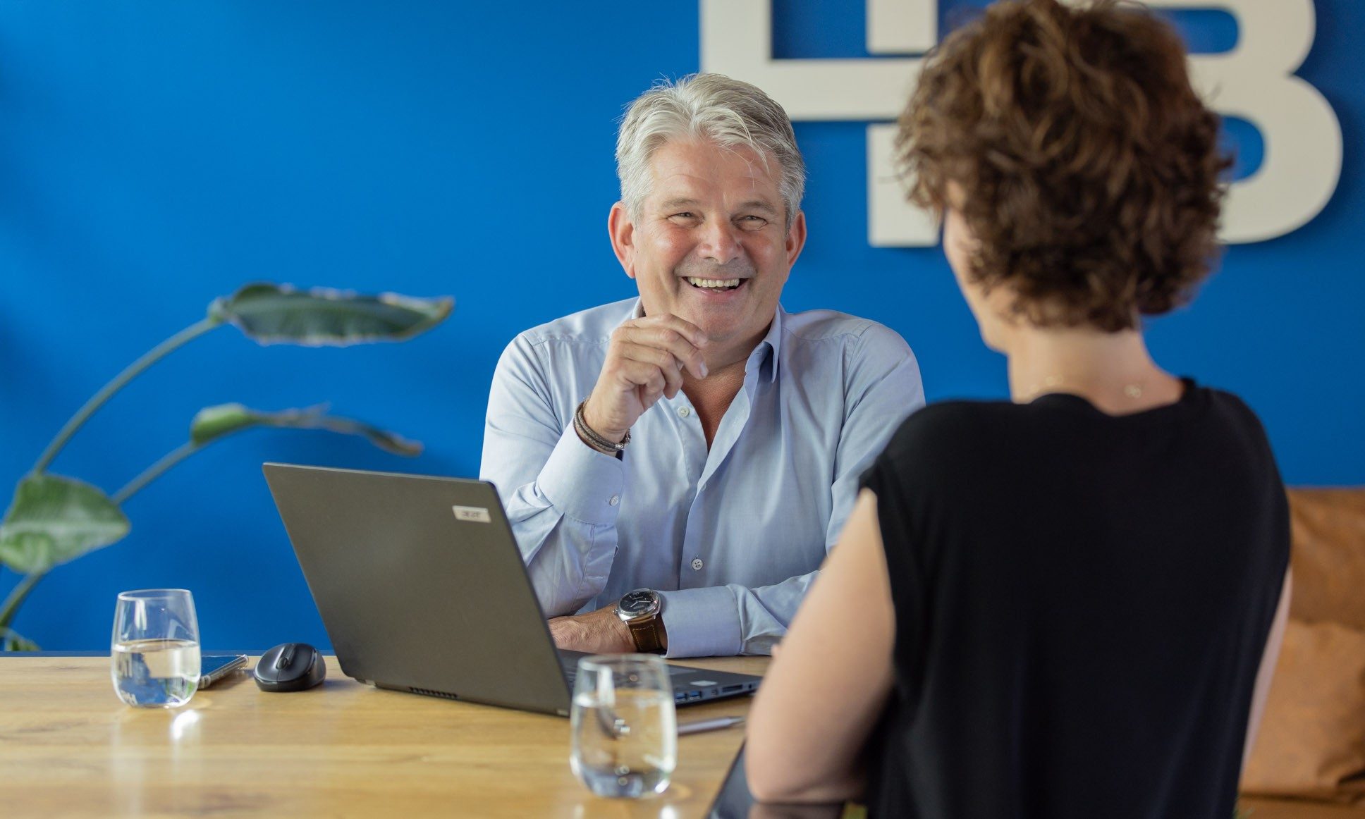 Twee mensen praten lachend aan een bureau met laptop.