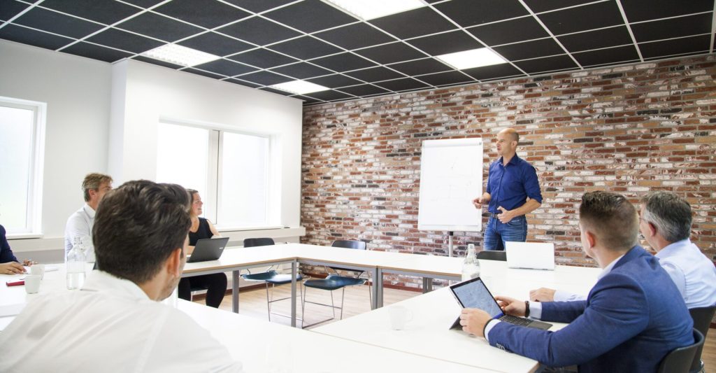 Presentatie in vergaderruimte met witte muren en stoelen.