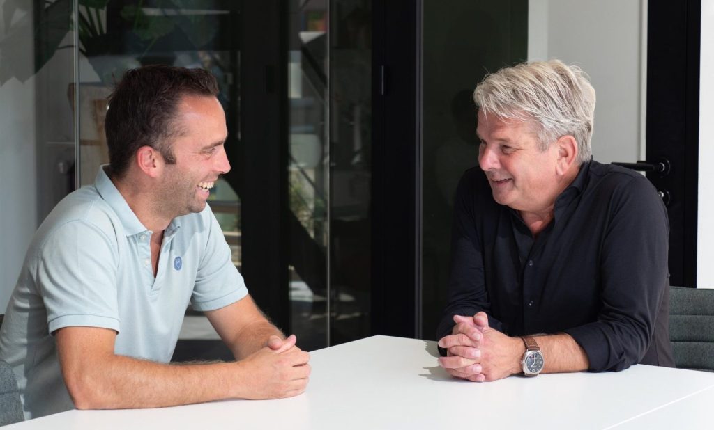 Twee mannen lachen tijdens een gesprek aan tafel.