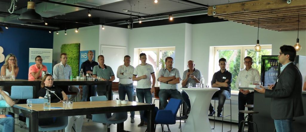 Groep mensen luistert naar presentatie in kantoorruimte.