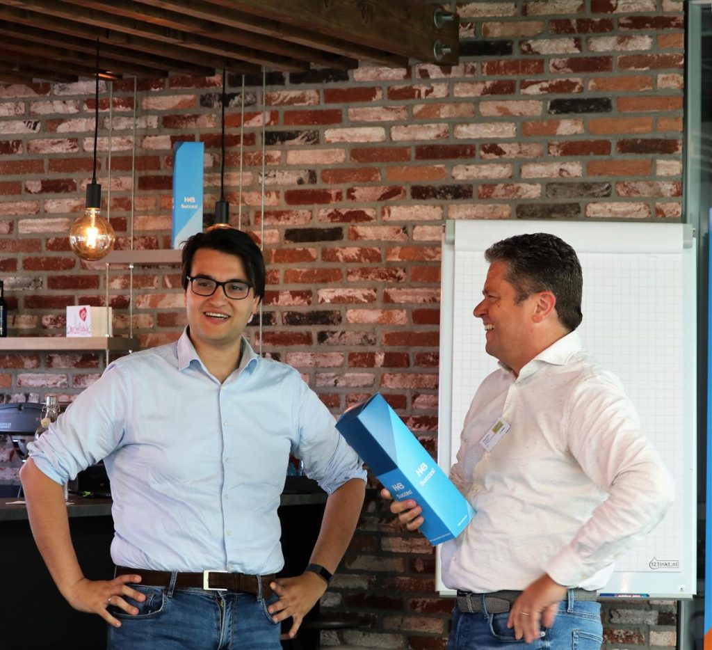 Twee mannen praten en lachen in een kantooromgeving.