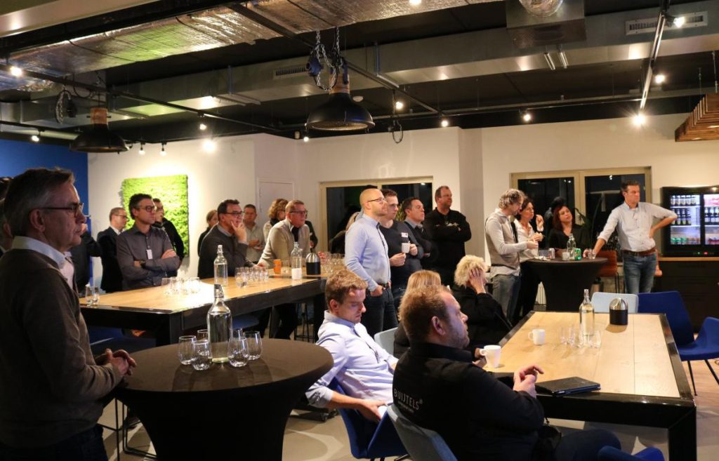 Groep mensen luistert naar presentatie in moderne ruimte.