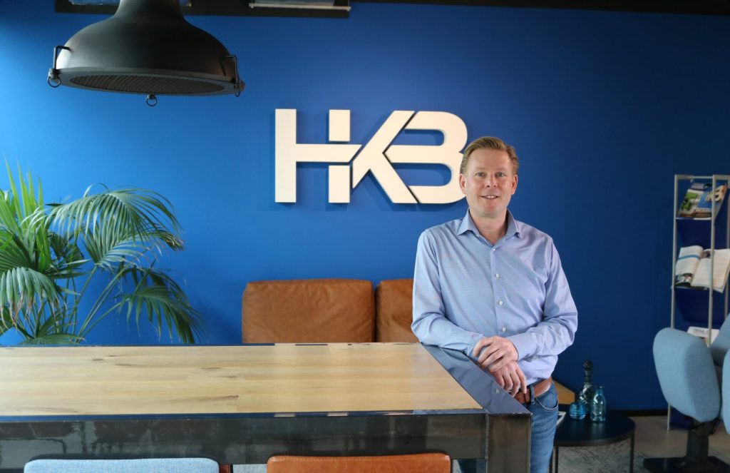 Man bij tafel in kantoor met HKB logo.