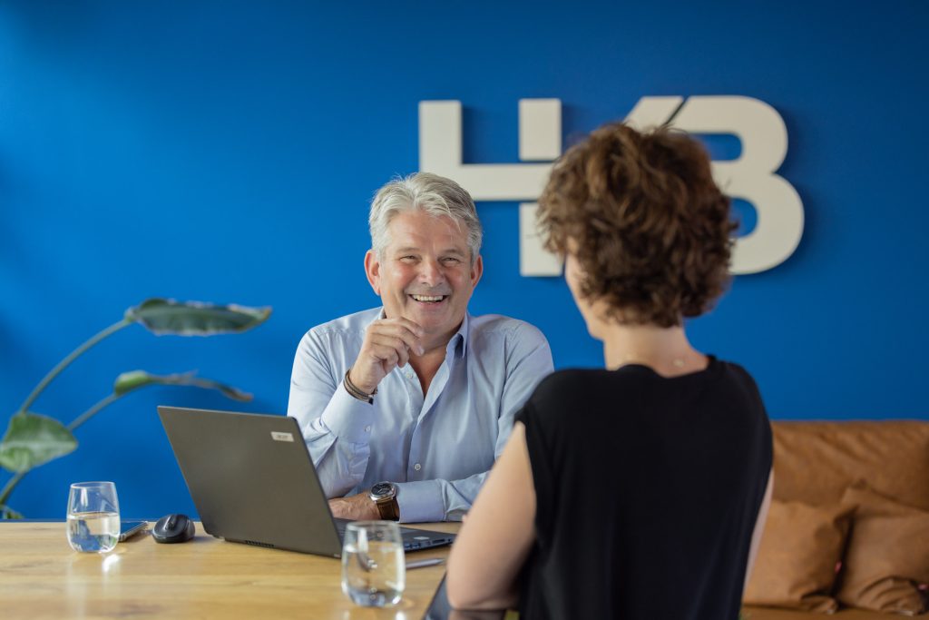 Twee mensen praten lachend bij bureau met laptop.