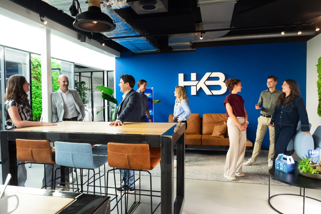 Groepsgesprek bij kantoorbureau met HKB-logo op muur.