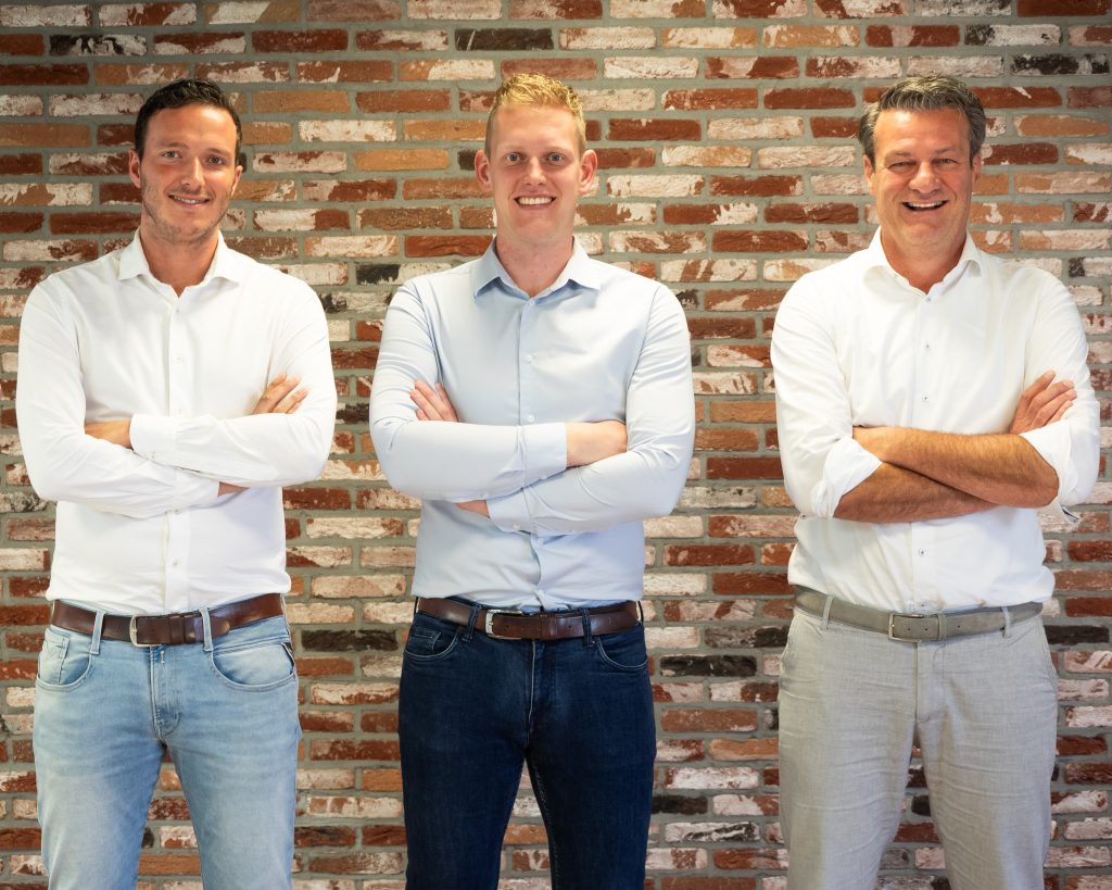 Drie mannen poseren voor bakstenen muur.