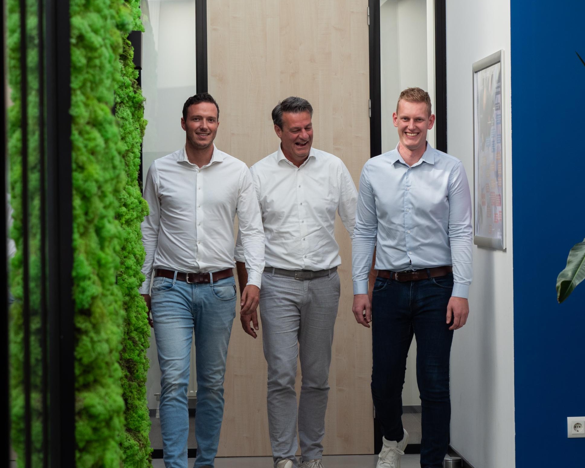 Drie mannen lopen lachend in een kantoor.