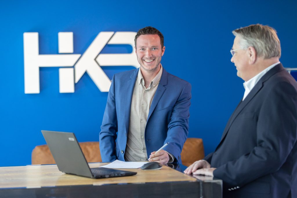 Twee mannen in gesprek bij laptop en bedrijfsmuur.