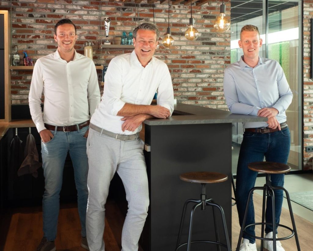 Drie lachende mannen in moderne kantoorruimte.