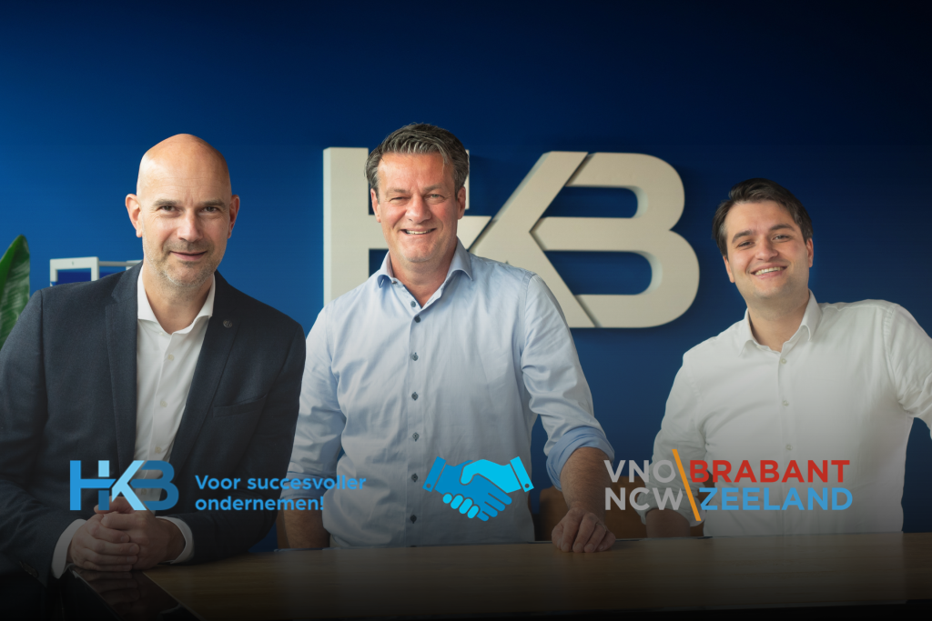 Drie mannen poseren voor blauw HK logo.